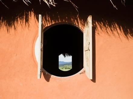 A round window cut into an adobe wall, looking out to the fields