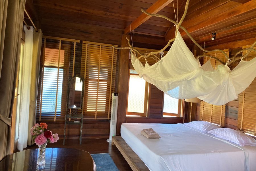 The teak house bedroom at Mala Dhara — a bed under a mosquito net, timber walls and windows onto the fields