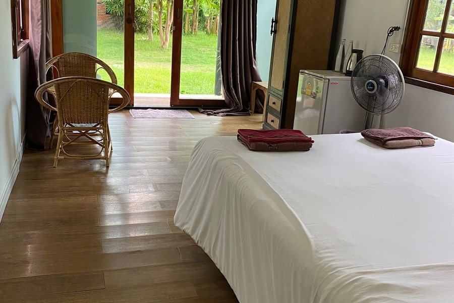 Inside the wooden bungalow at Mala Dhara — a bed on a timber floor with doors open to the garden